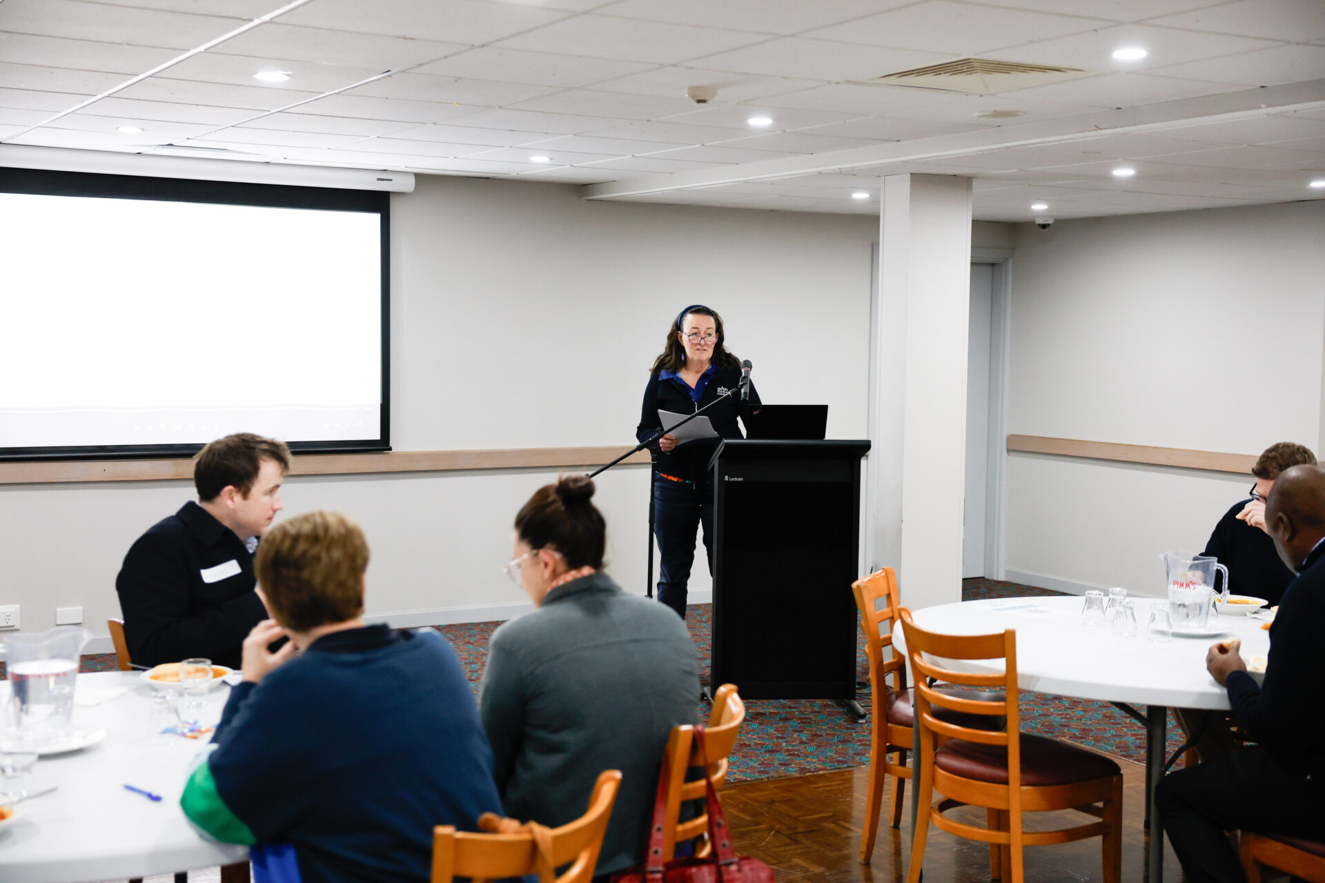 WNSW PHN staff member delivering a presentation in front of healthcare professionals in a room with a presentation screen.