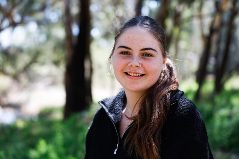 Portrait of girl sitting in a natural setting with grass and trees in the background.