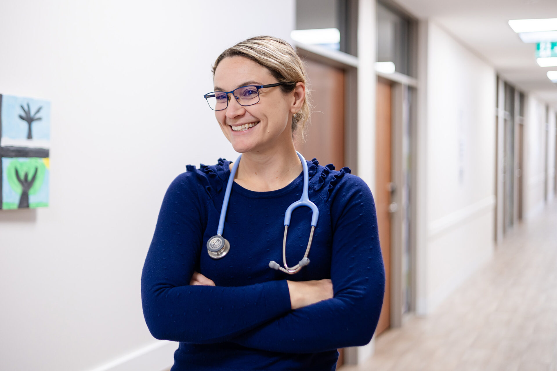 General Practitioner standing in a clinic hallway smiling with her arms crossed.