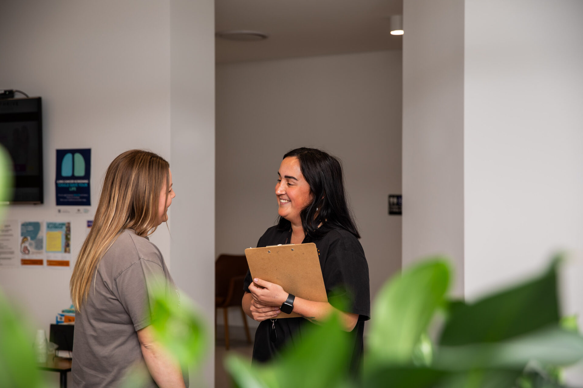Healthcare professional greeting a patient in the waiting room of a clinic with green plant in foreground.