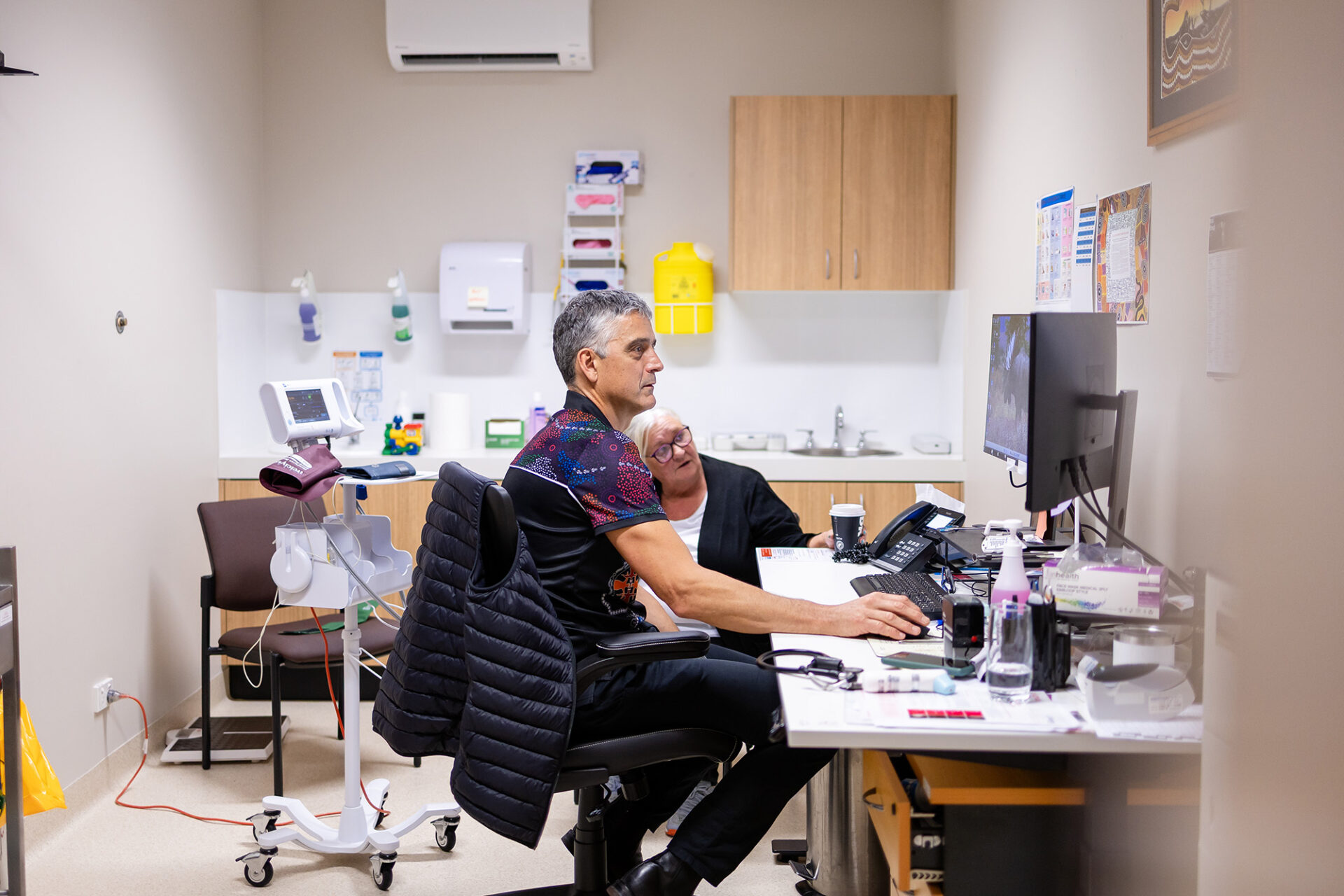 General Practitioner in consult room with a patient showing her something on the computer.