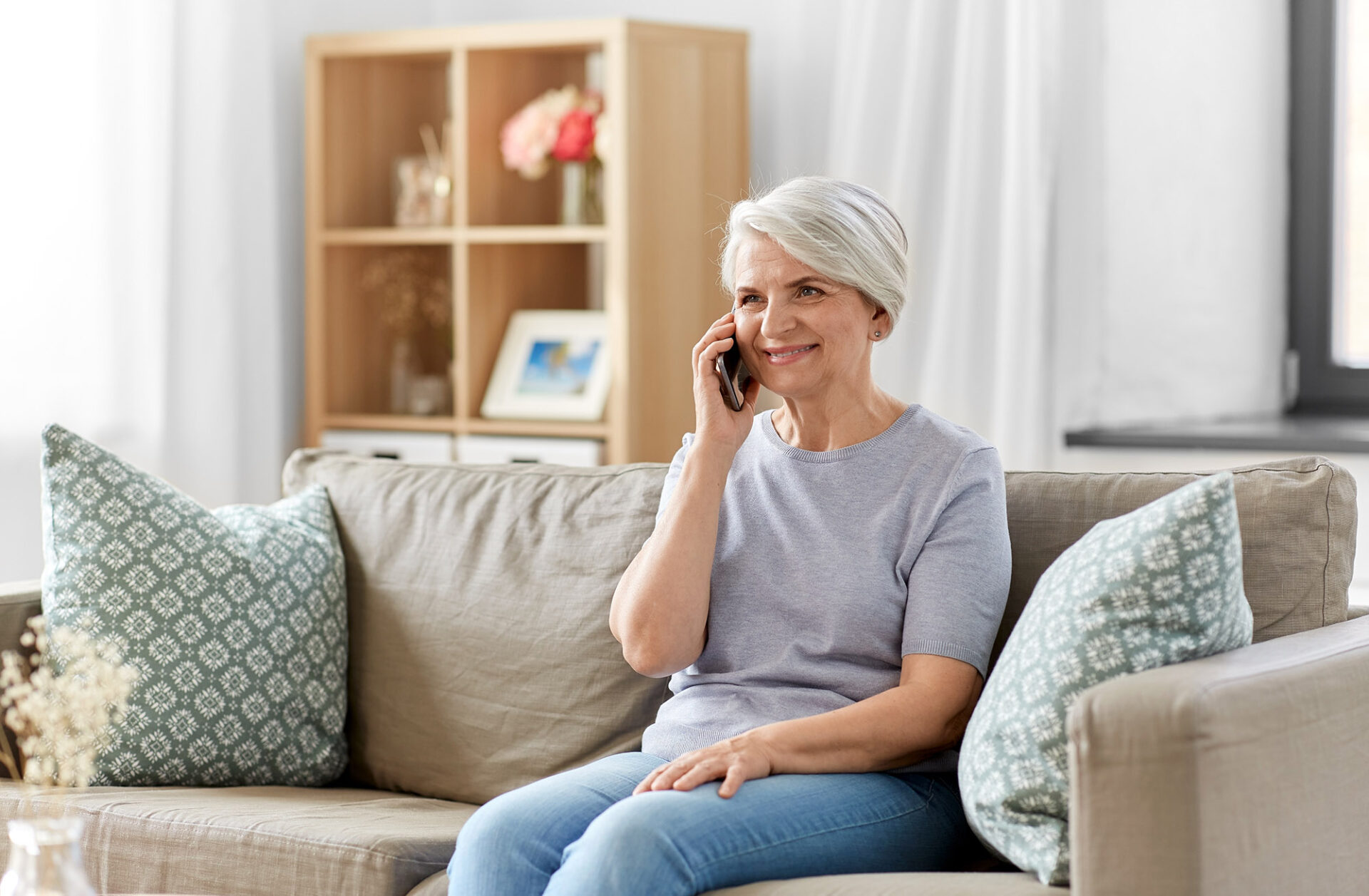 Older woman sitting on a couch smiling while talking on a mobile phone.
