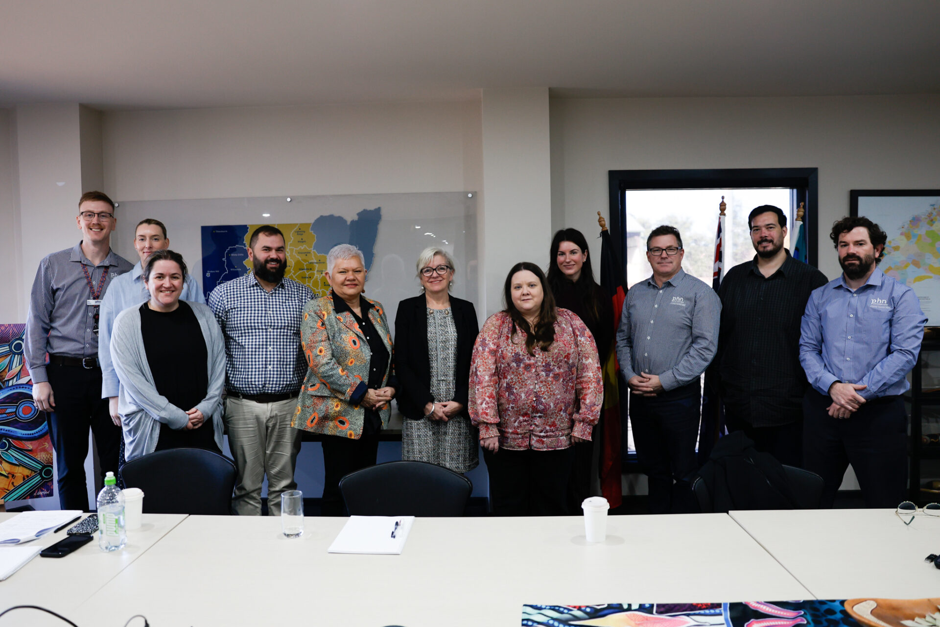 Photograph of a group of ten people standing behind a conference table in a meeting room, smiling and posing for the camera.