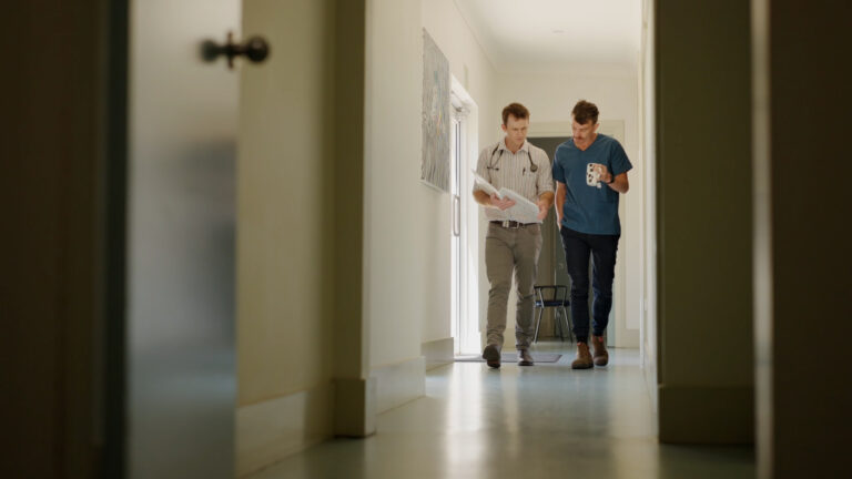 Two General Practice doctors walking down the hall talking to each other reading a patient file