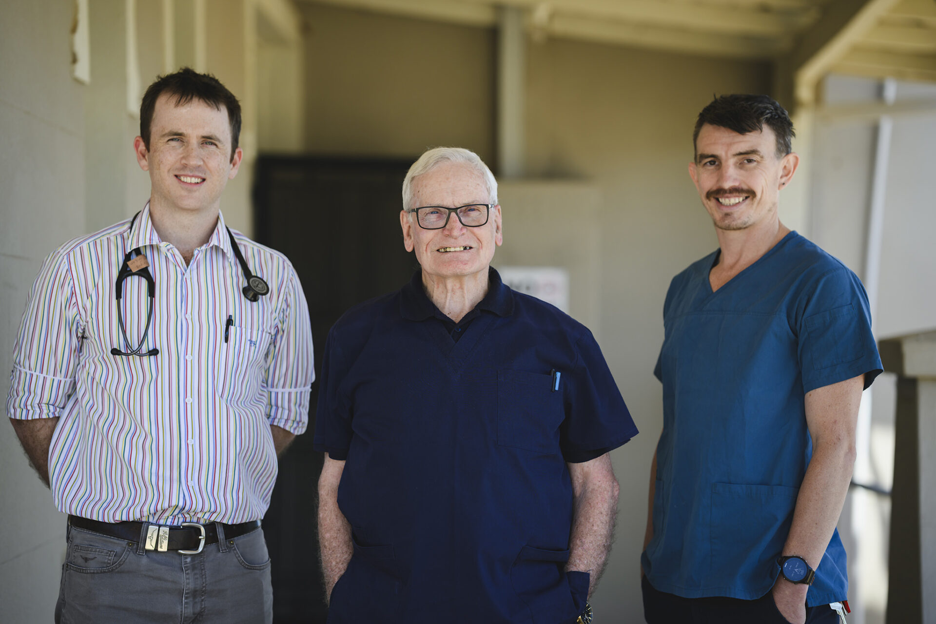 Two young male GP Registrars with an older male doctor under a verandah