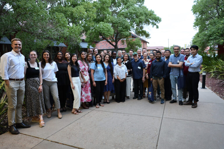 Large group of professional people standing together looking at the camera smiling on a cement path with trees behind