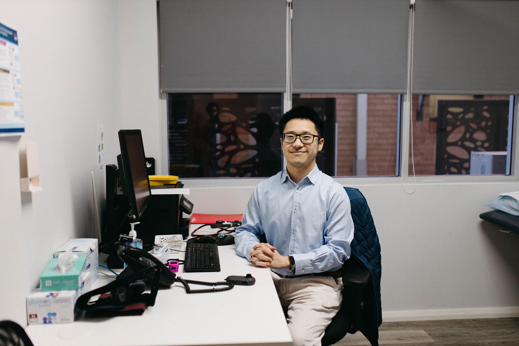 Male GP sitting at his desk smiling at the camera