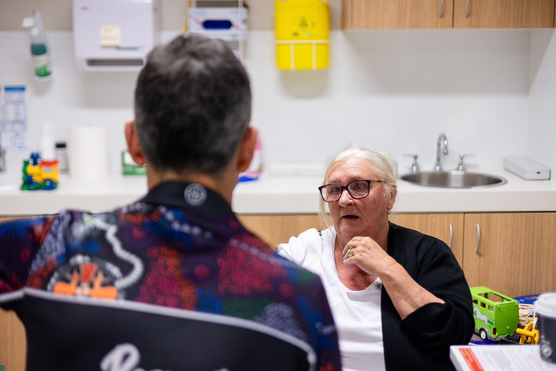 Female older patient talking seriously with a male GP whose back is to the camera.